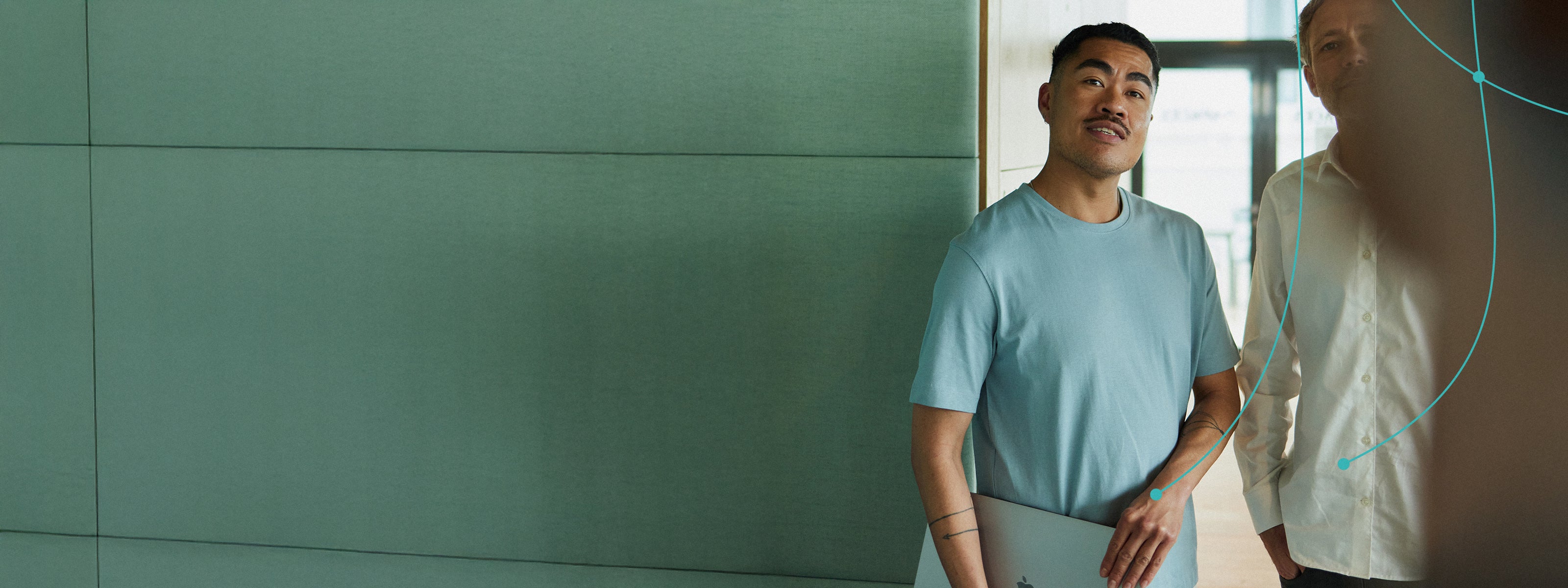 Two men looking at the camera, one holding a laptop in a professional setting