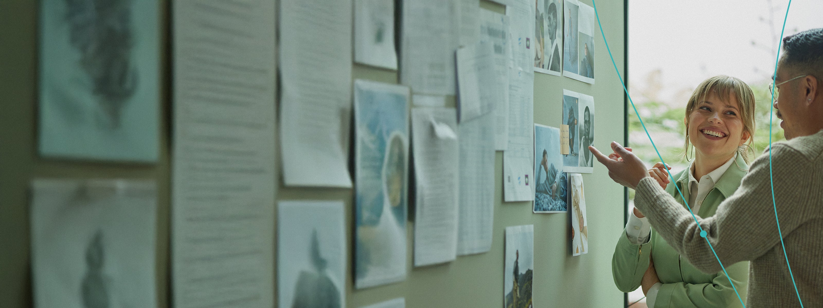 People smiling and talking in front of a wall covered with papers, suggesting collaboration in a creative workspace