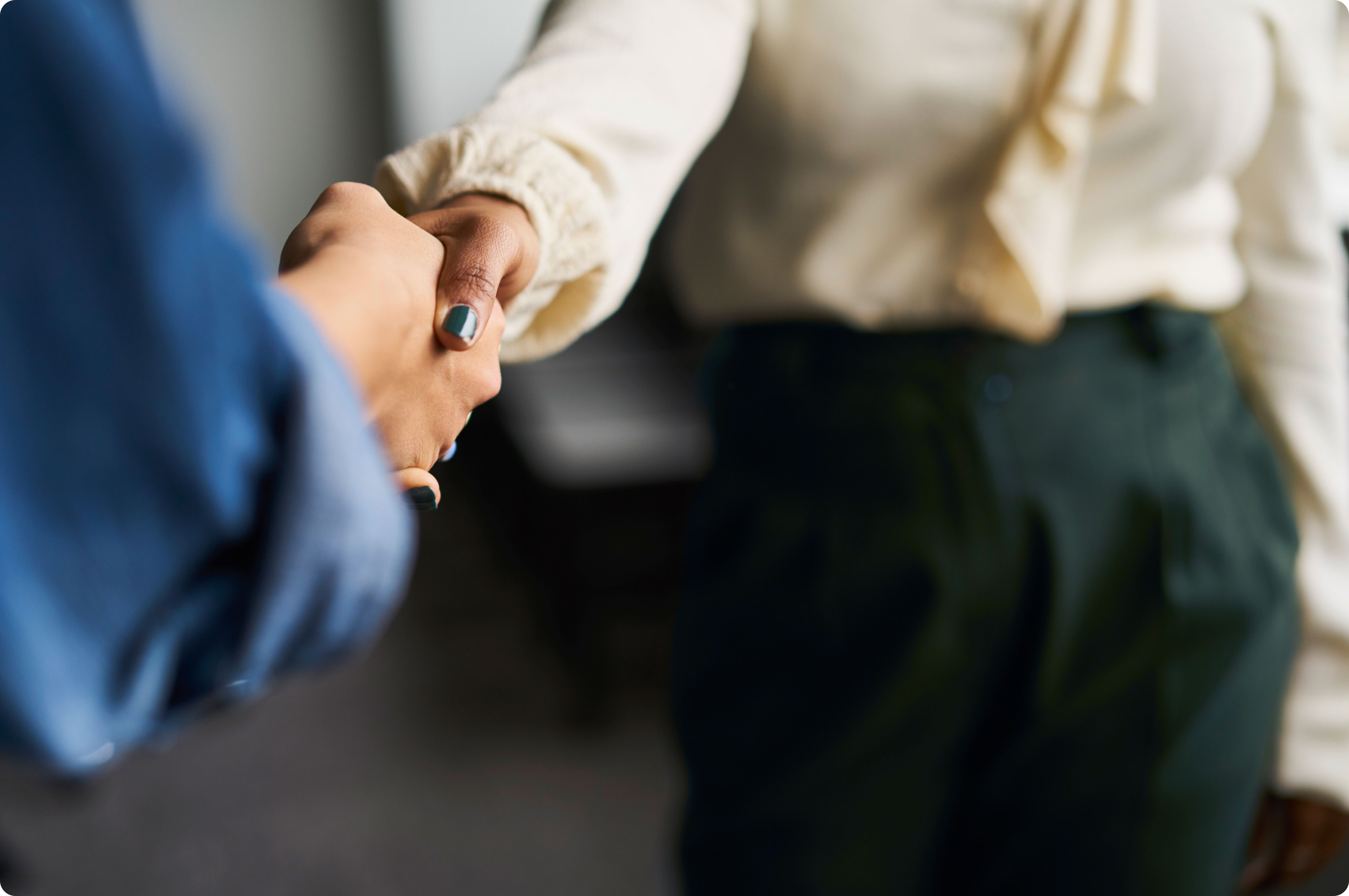 A business woman in a white shirt shaking hands with a coworker in a blue shirt.